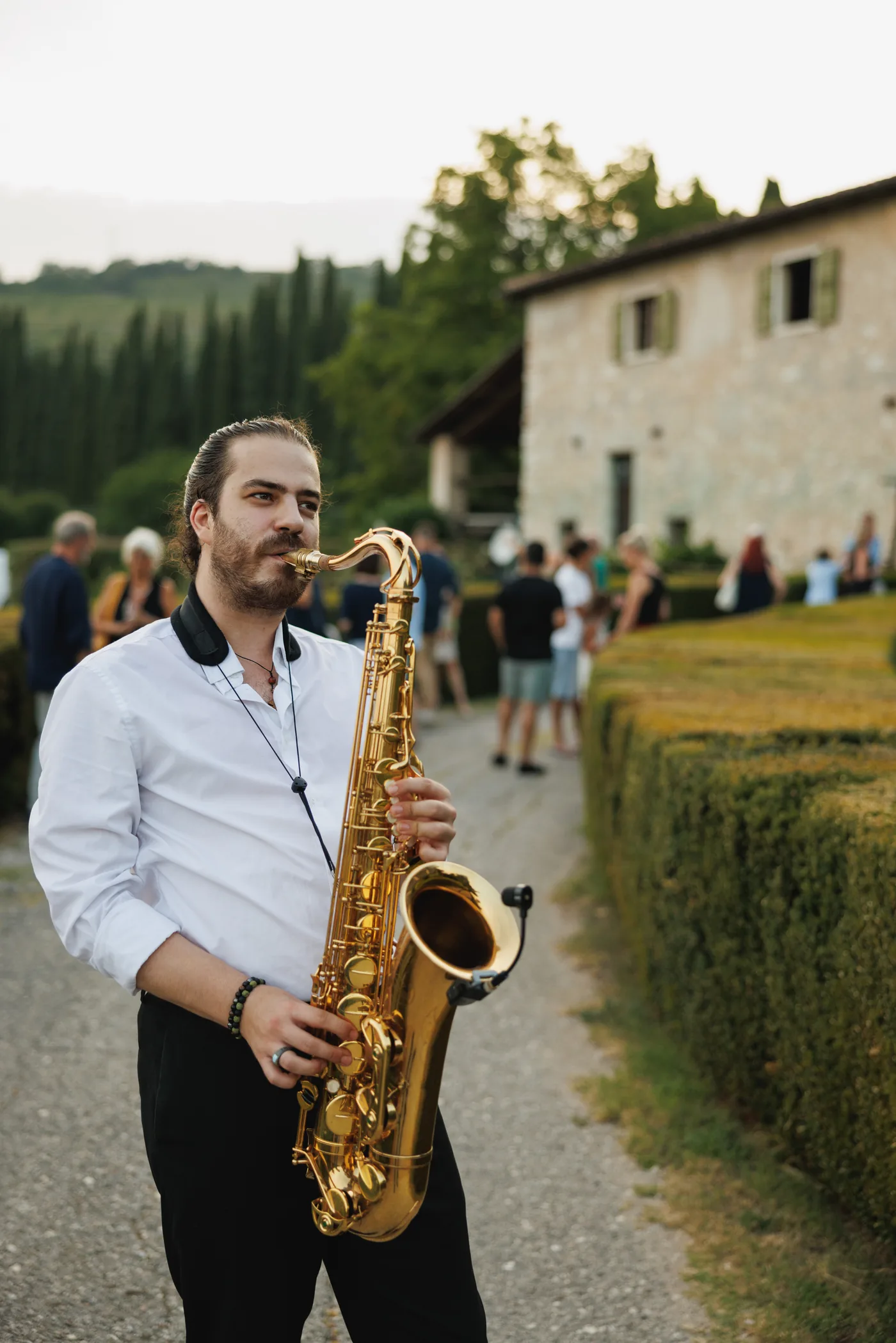 Pietro suona il sax all'aperitivo, fra gli invitati, davanti a una villa